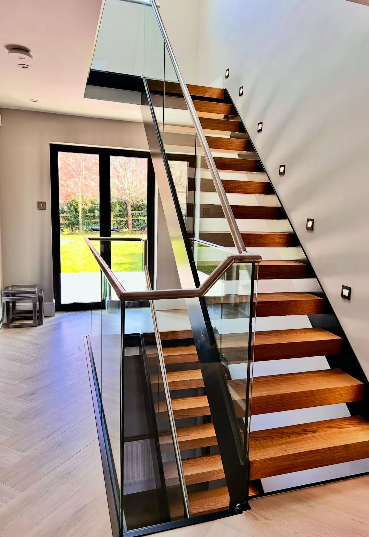 Glass staircase balustrade with frameless panels illuminating a light-filled hallway